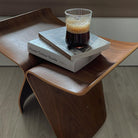 Pootoo's Butterfly Stool paired with books and coffee, showcasing a leisurely lifestyle. The stool's elegant design complements the warm wood, making it ideal for enjoying reading time in a cozy corner.